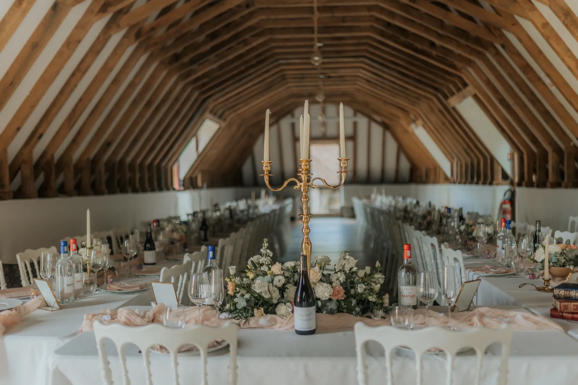Salle de réception de mariage à Pau, décorée avec tables élégantes, fleurs blanches et chandelier sous charpente en bois