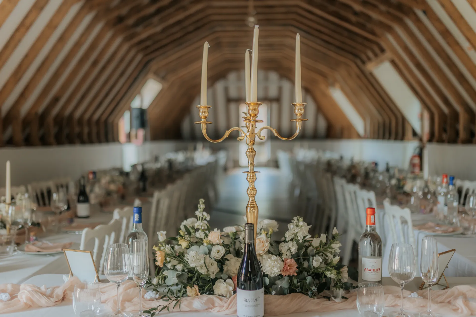 Salle de réception de mariage élégante à Pau, décorée de fleurs blanches et chandelier doré sous charpente en bois