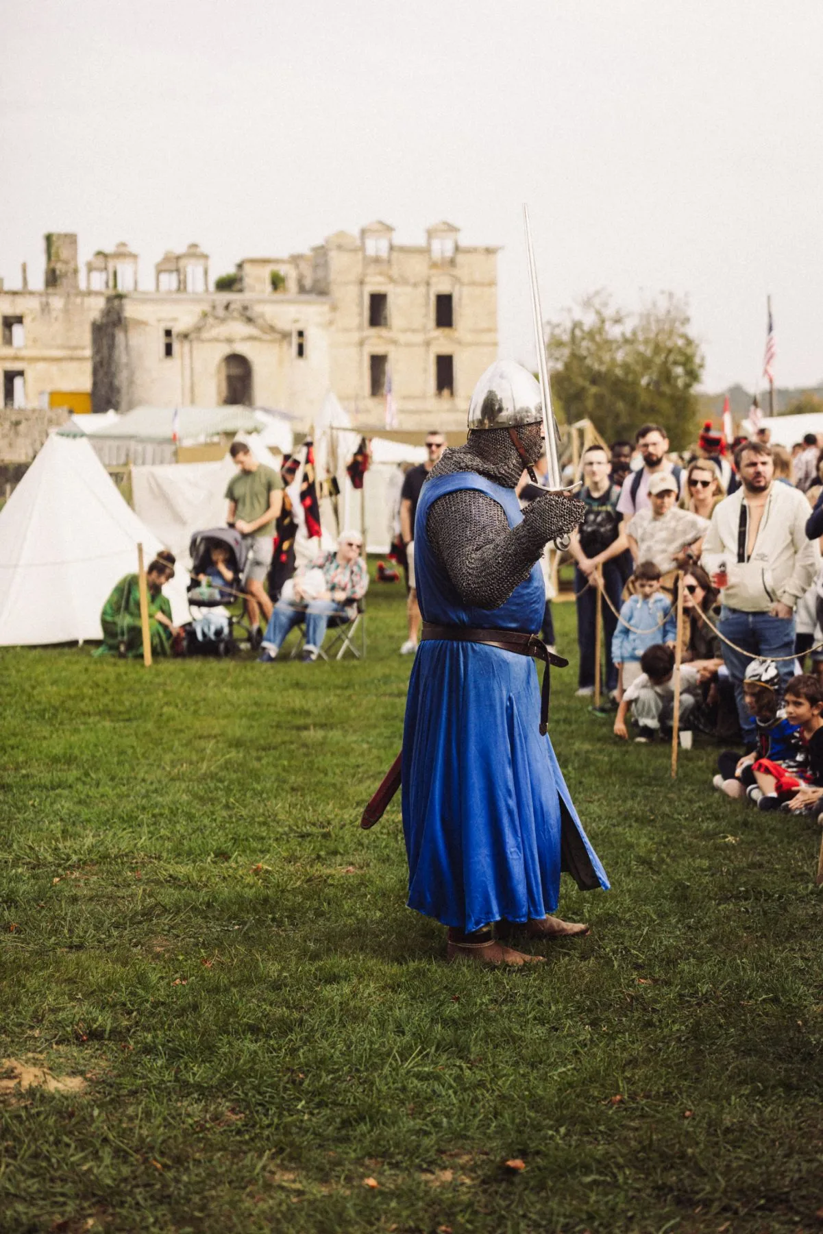 Chevalier en armure bleue lors d’une reconstitution médiévale au Château de Bidache, devant le public et les tentes