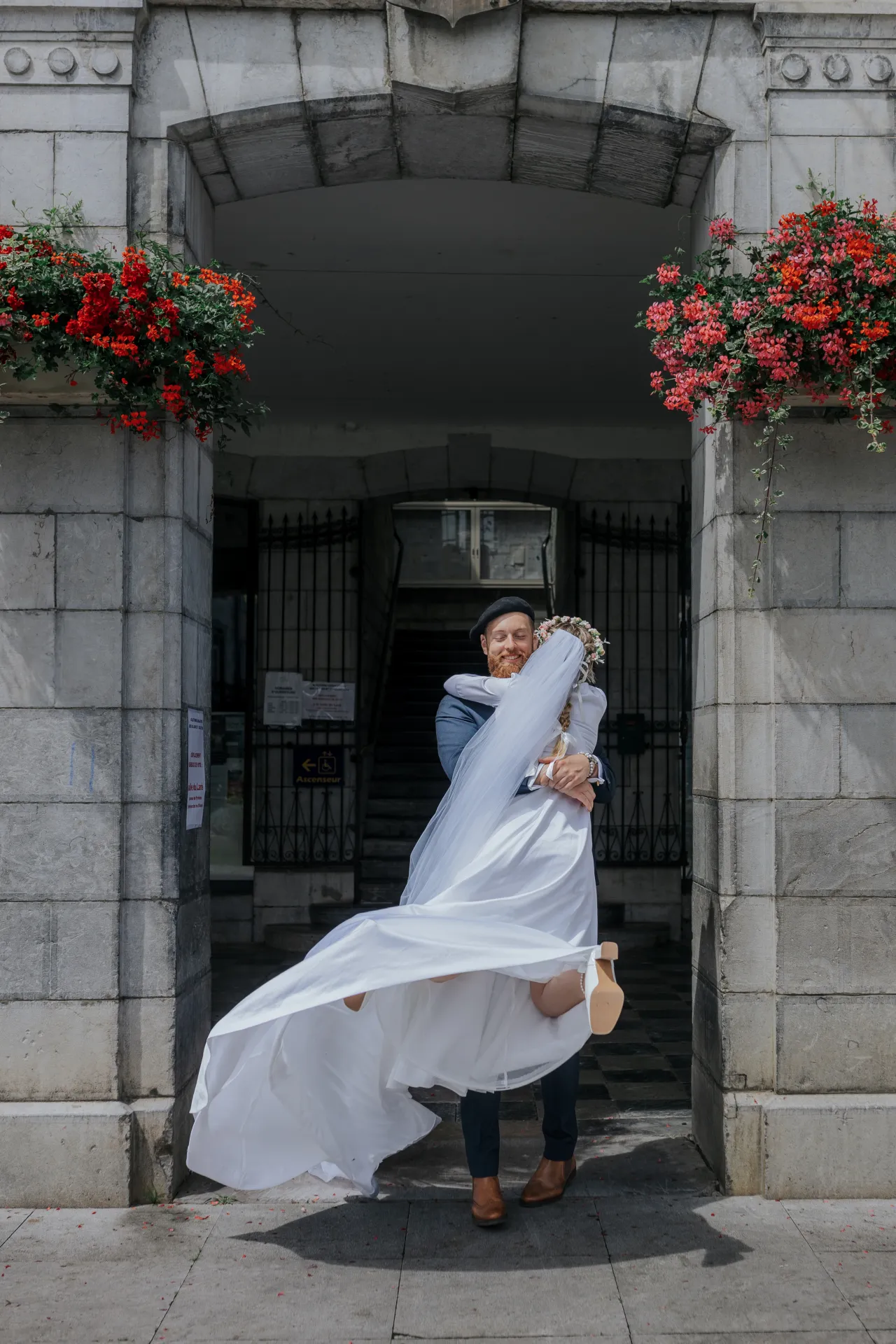 Mariés enlacés devant la mairie d’Arudy, voile au vent, lors d’un mariage intimiste dans les Pyrénées-Atlantiques