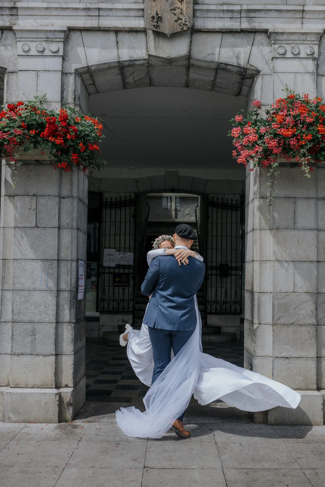 Mariés s’enlaçant devant la mairie d’Arudy, voile au vent, lors d’un mariage intimiste dans les Pyrénées-Atlantiques