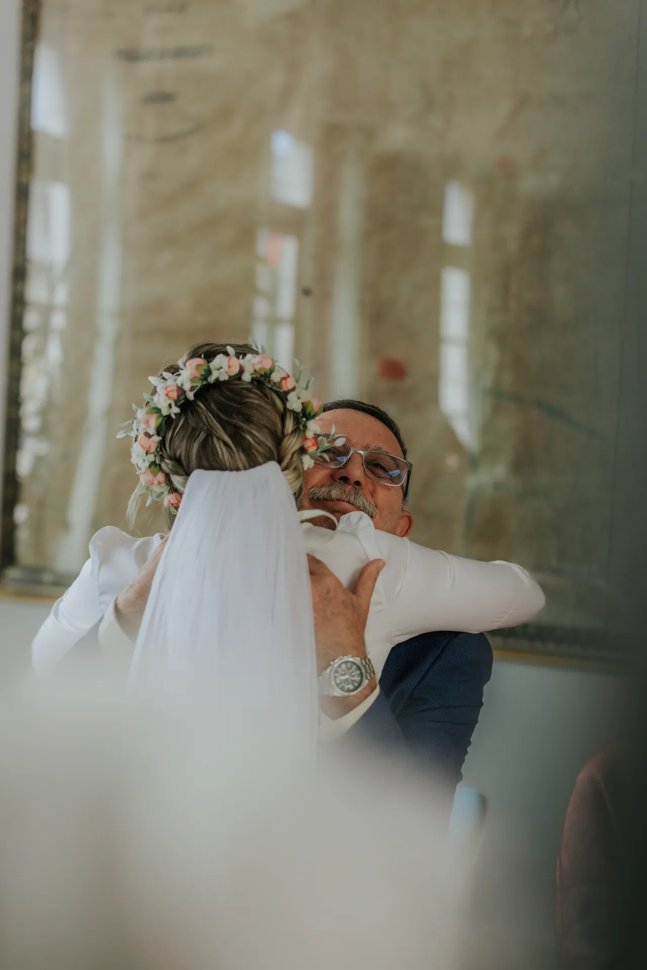 Mariée enlacée par un proche à la mairie d’Arudy lors d’un mariage intimiste, voile et couronne de fleurs