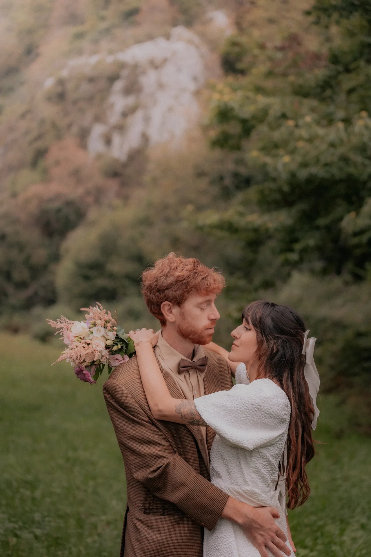 Couple de mariés enlacés en pleine nature à Pau, ambiance vintage et romantique, bouquet pastel et falaise en arrière-plan