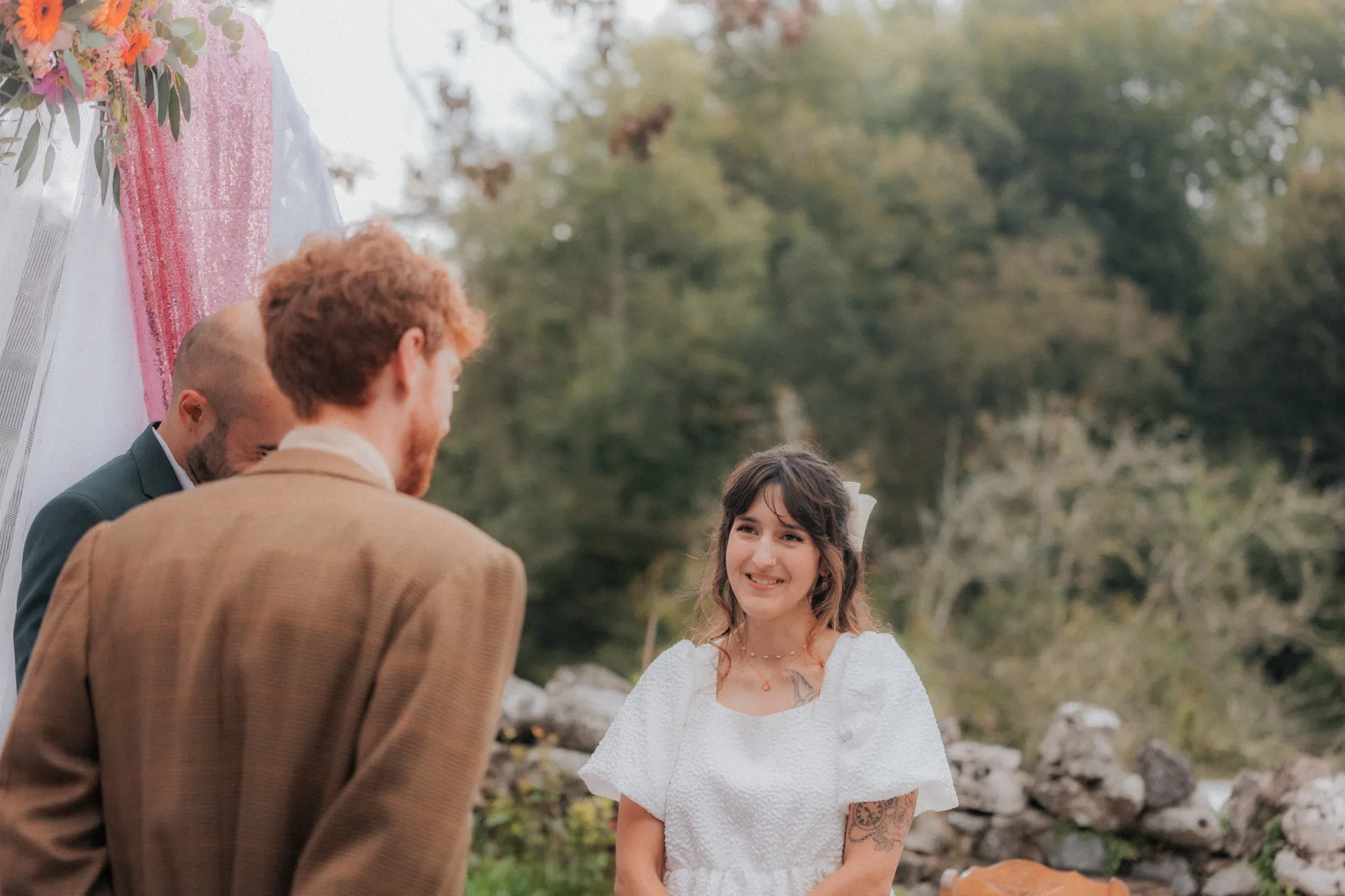 Cérémonie de mariage vintage en pleine nature à Pau, mariée souriante face à son partenaire sous une arche fleurie