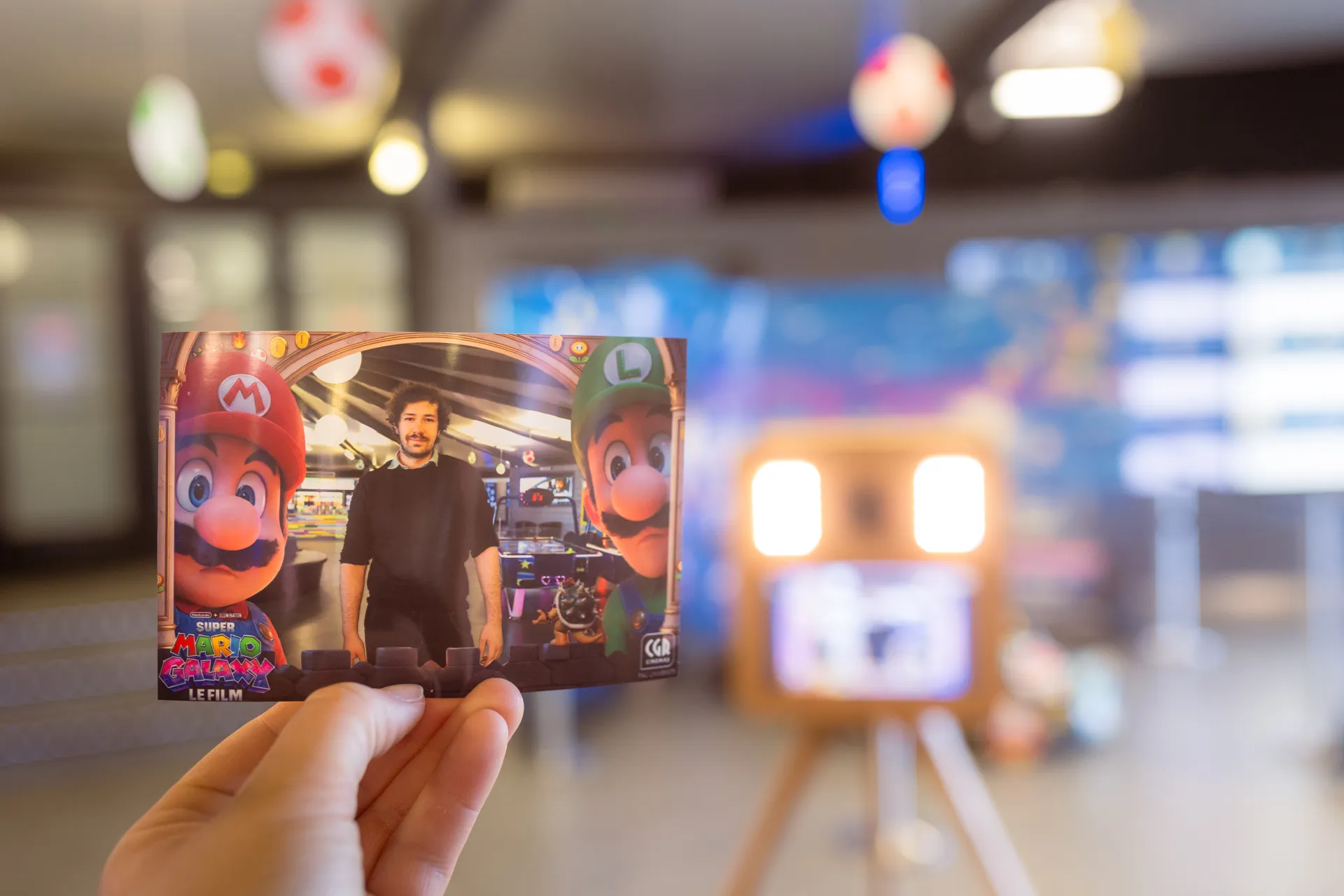 Tirage photo du photobooth Mario Galaxy au CGR Pau Université, tenu en main devant la borne floutée en arrière-plan