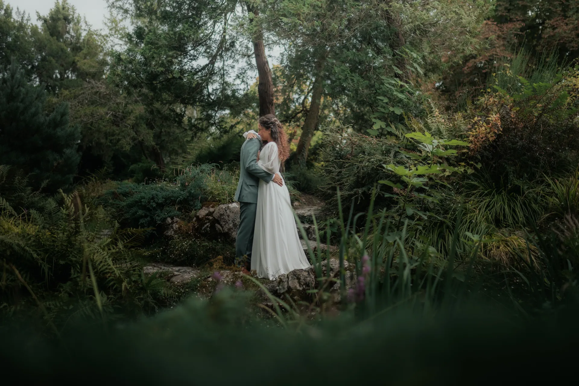 Couple de mariés enlacés dans un jardin luxuriant au Théâtre de Verdure, séance photo de mariage à Pau