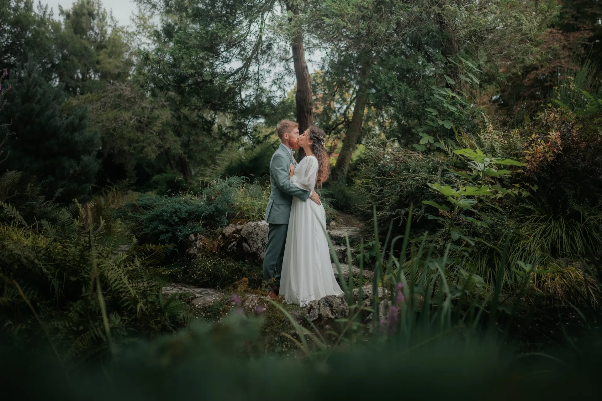 Couple de mariés s’embrassant dans un jardin luxuriant au Théâtre de Verdure, séance photo de mariage à Pau