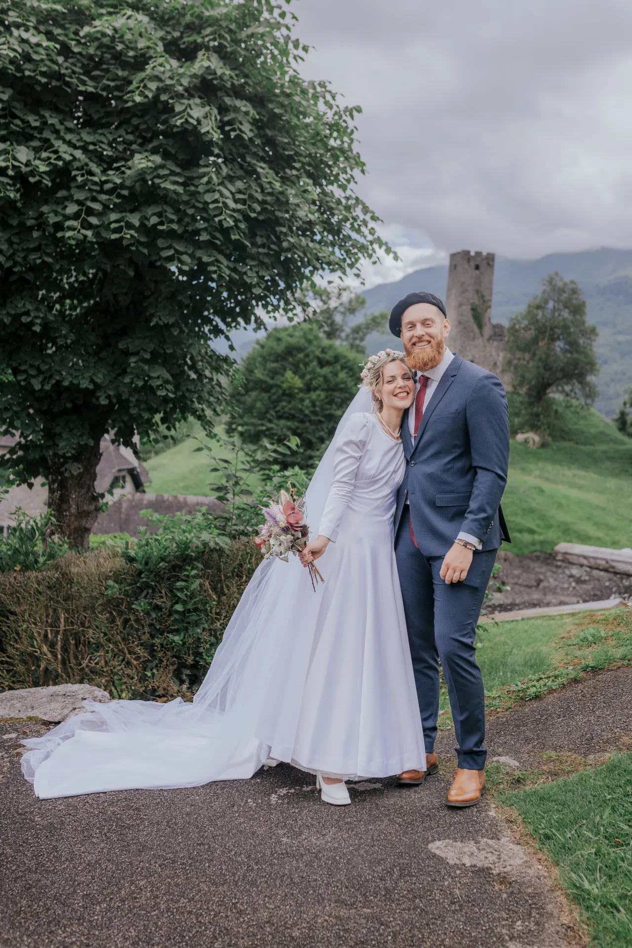 Mariés souriants à Castet devant l’Église Saint-Polycarpe, séance couple au cœur d’un paysage verdoyant