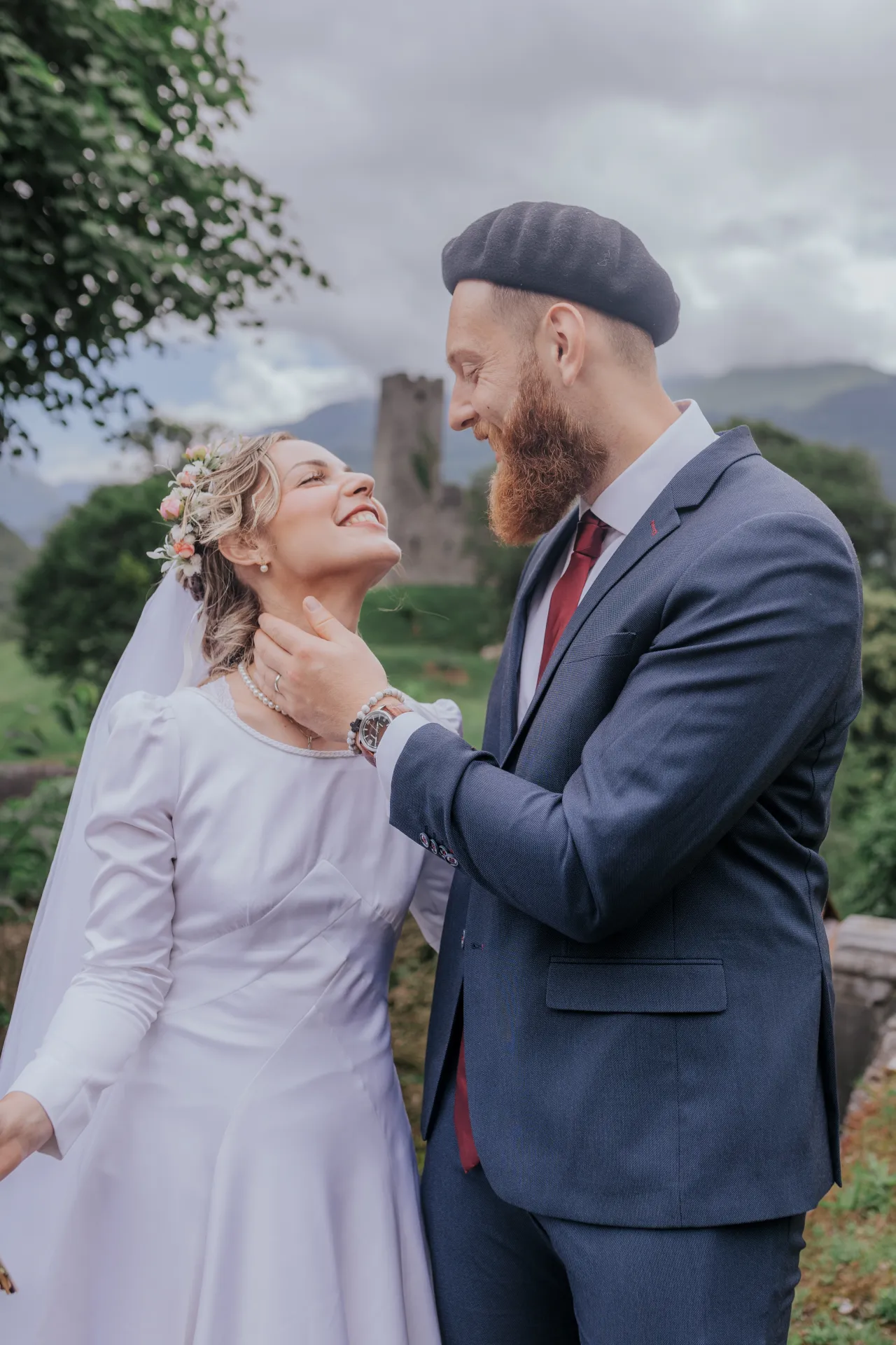 Mariés souriants en séance couple à Castet près de l’Église Saint-Polycarpe, avec les montagnes en arrière-plan