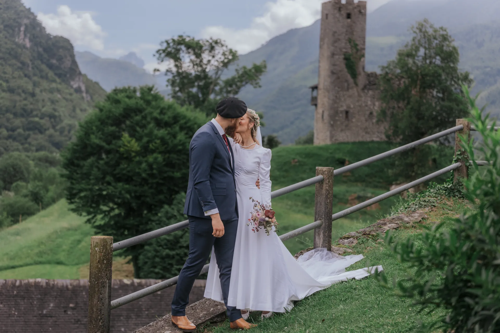 Mariés s’embrassant à Castet près de l’Église Saint-Polycarpe, avec montagne et tour en fond
