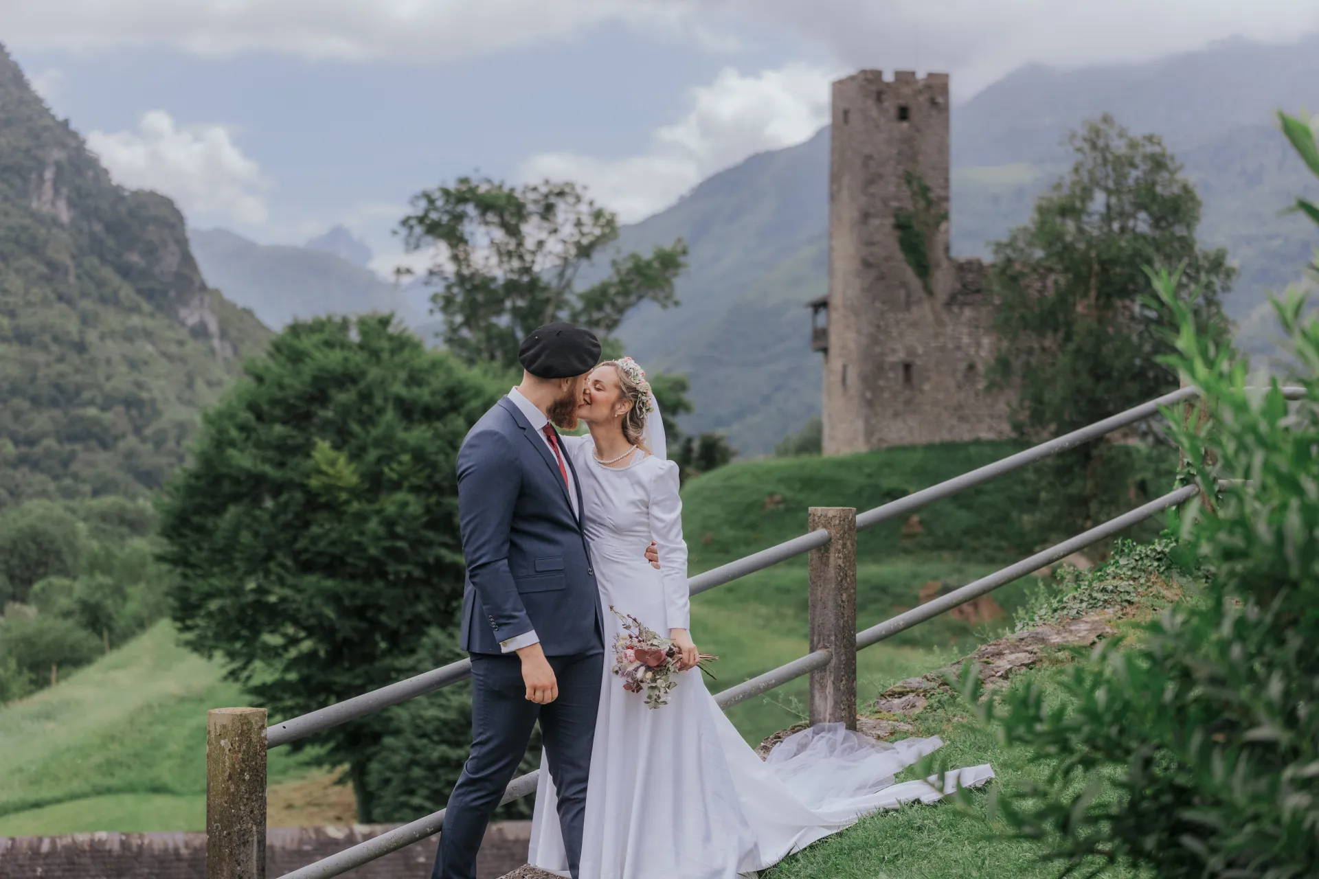 Couple de mariés s’embrassant à Castet devant l’Église Saint-Polycarpe, avec vue sur les montagnes béarnaises