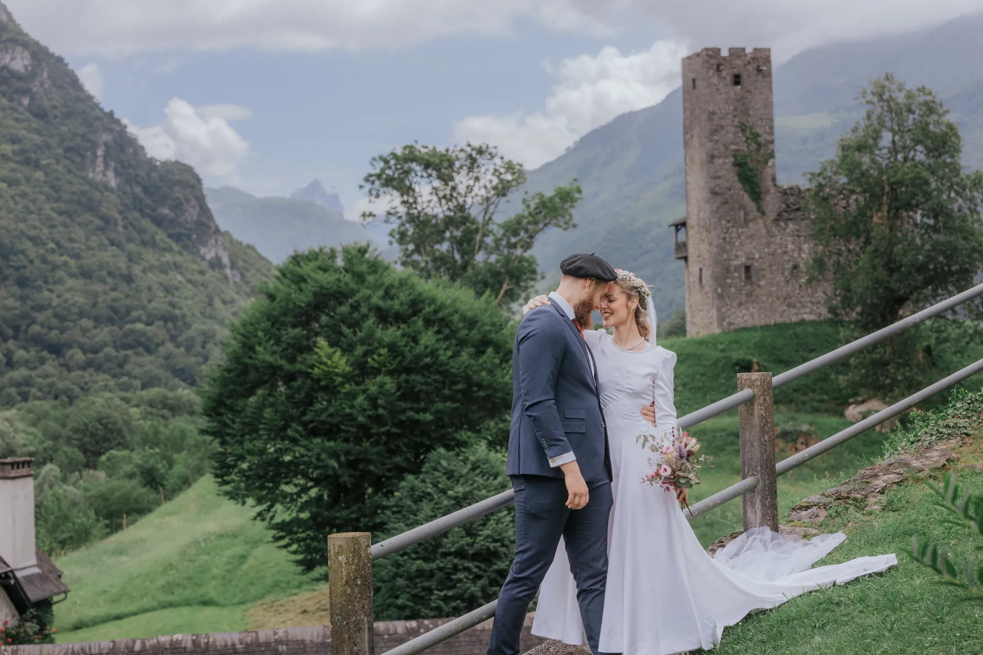 Mariés en séance couple à Castet, près de l’Église Saint-Polycarpe, avec vue sur les montagnes et une tour en pierre
