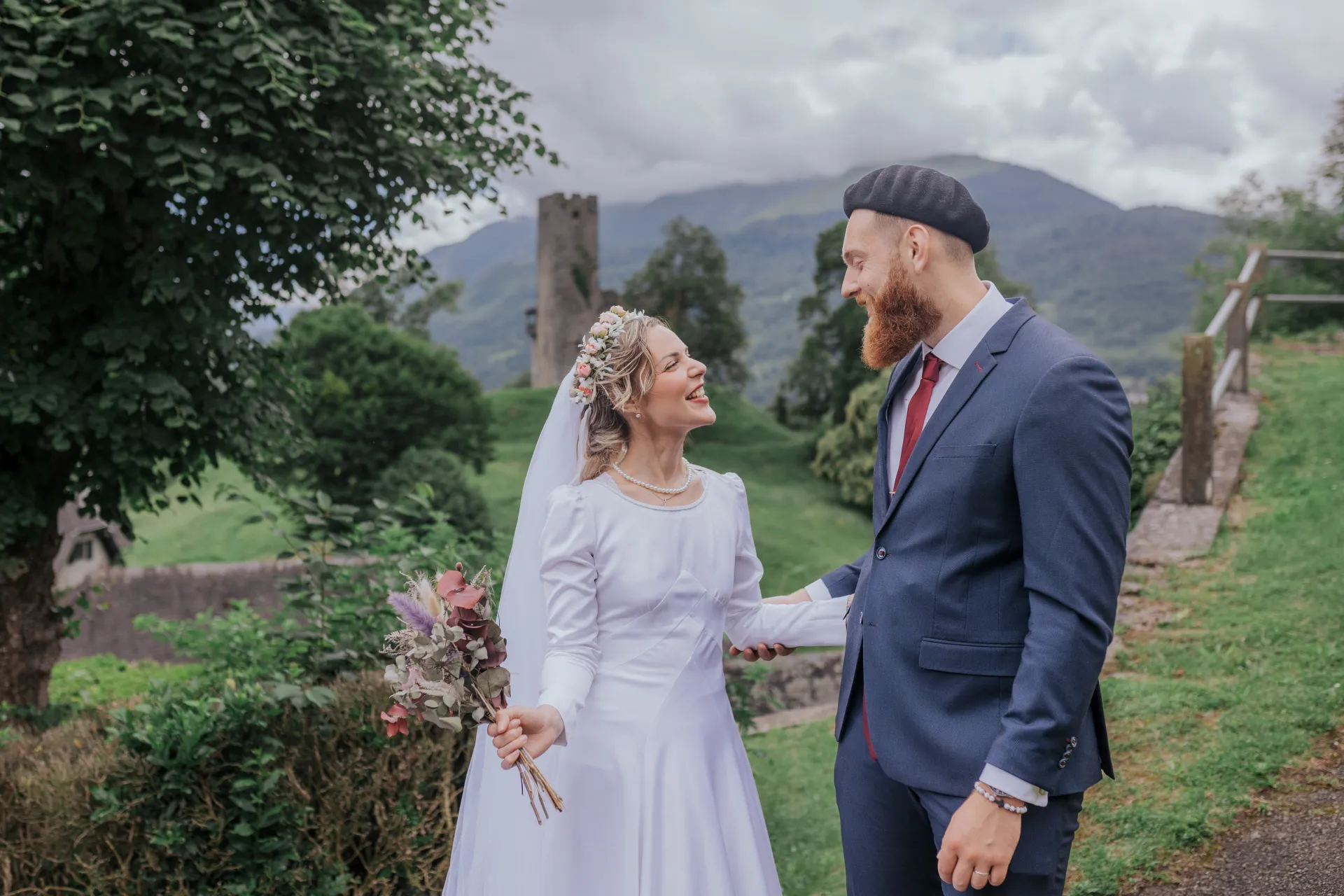 Mariés souriants en séance couple à Castet près de l’église Saint-Polycarpe, avec vue sur les montagnes béarnaises