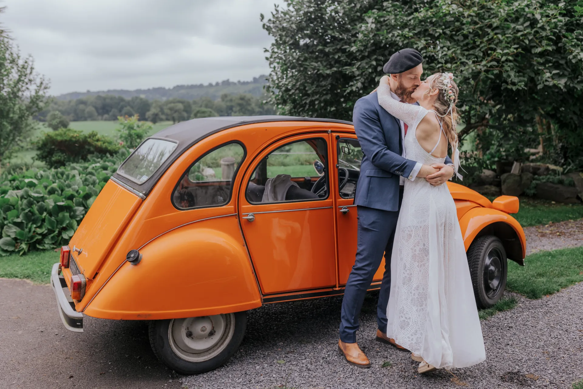 Mariés s’embrassant près d’une voiture vintage orange à Castet, séance couple après le mariage à l’Église Saint-Polycarpe