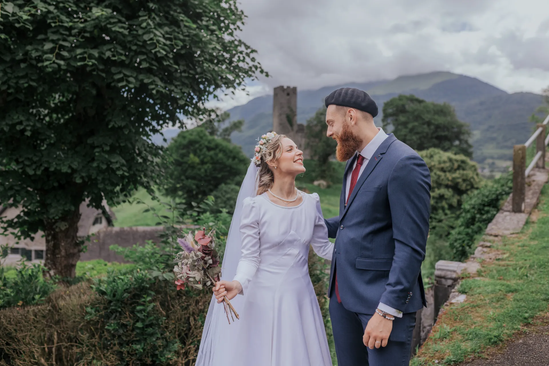 Mariés souriants en séance couple à Castet près de l’Église Saint-Polycarpe, avec vue sur les montagnes béarnaises