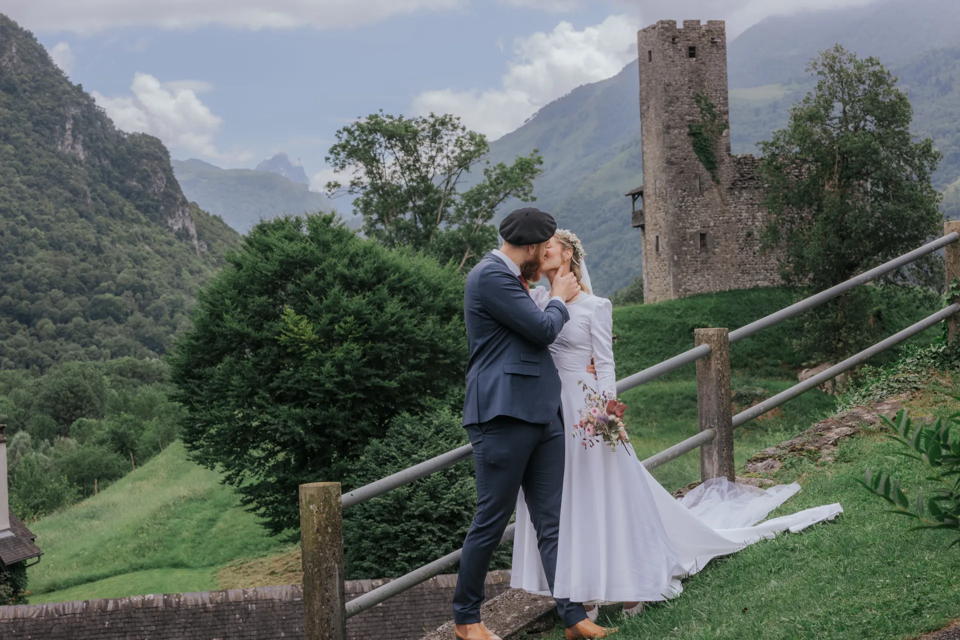 Mariés s’embrassant à Castet près de l’Église Saint-Polycarpe, avec vue sur les montagnes et une tour en pierre