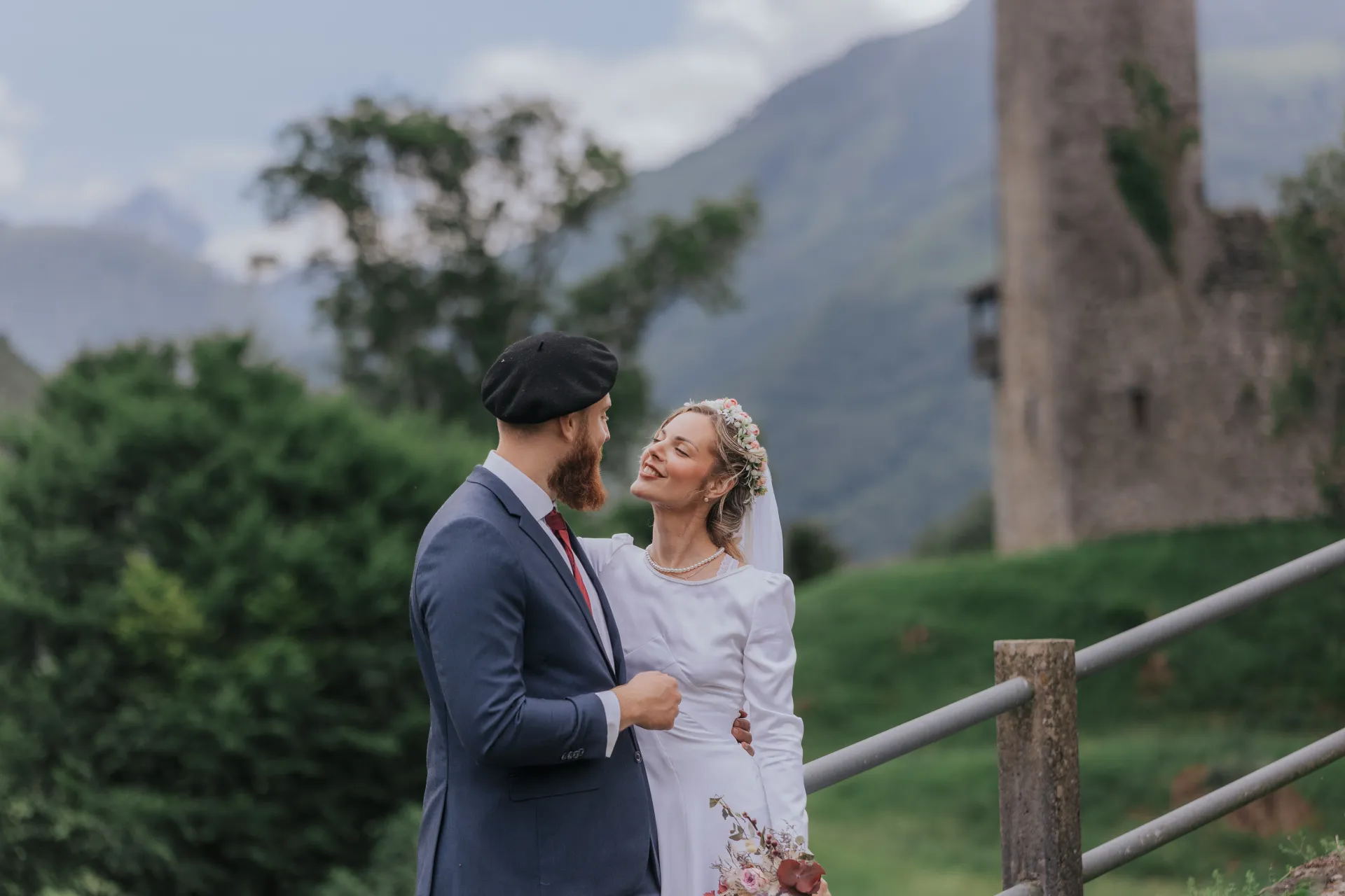 Mariés en séance couple à Castet près de l’Église Saint-Polycarpe, avec montagnes et tour en arrière-plan