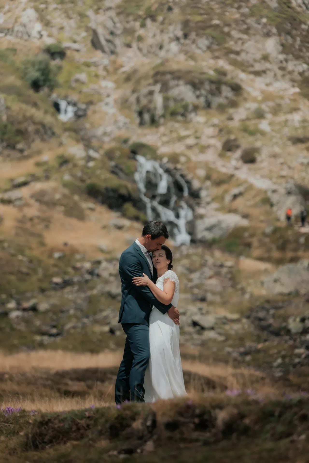 Couple de mariés enlacés en séance Day After aux Lacs d’Ayous, face à une cascade en montagne dans les Pyrénées-Atlantiques