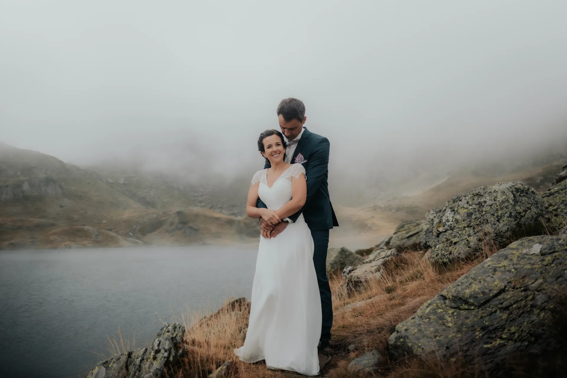 Couple marié enlacé au bord d’un lac brumeux aux Lacs d’Ayous, séance day after en montagne dans les Pyrénées-Atlantiques