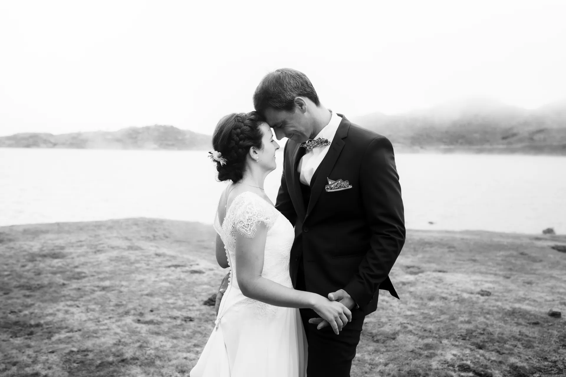 Photo de couple de mariés enlacés dans le brouillard aux Lacs d’Ayous, avec paysage de montagne flou en arrière-plan