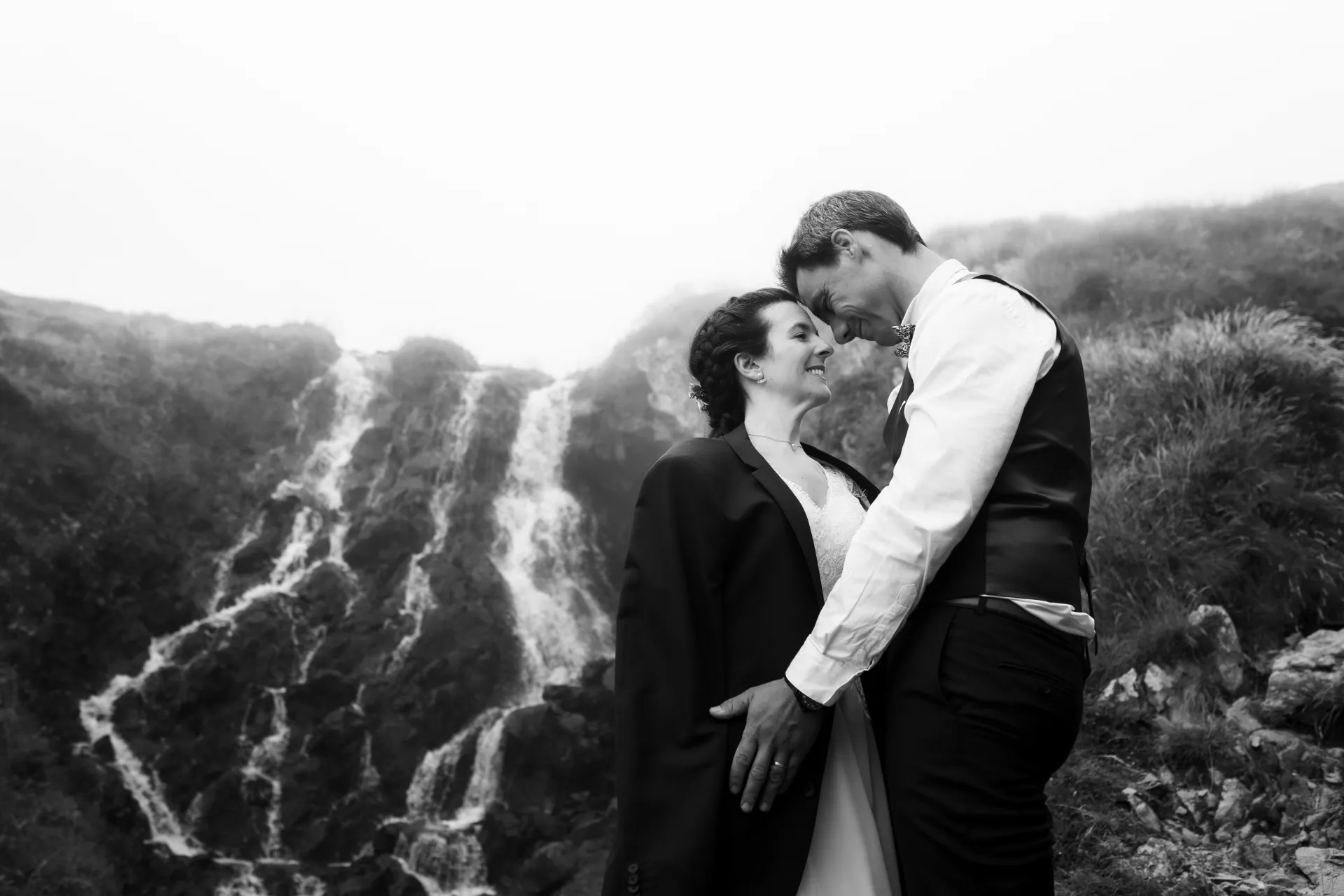 Couple de mariés en séance Day After aux Lacs d’Ayous, enlacés devant une cascade en montagne dans les Pyrénées-Atlantiques