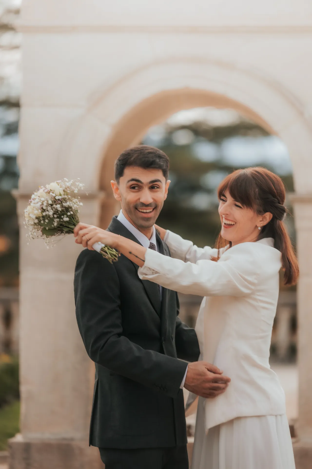 Couple de mariés souriant sous une arche à Pau, séance photo mariage romantique sur le Boulevard des Pyrénées