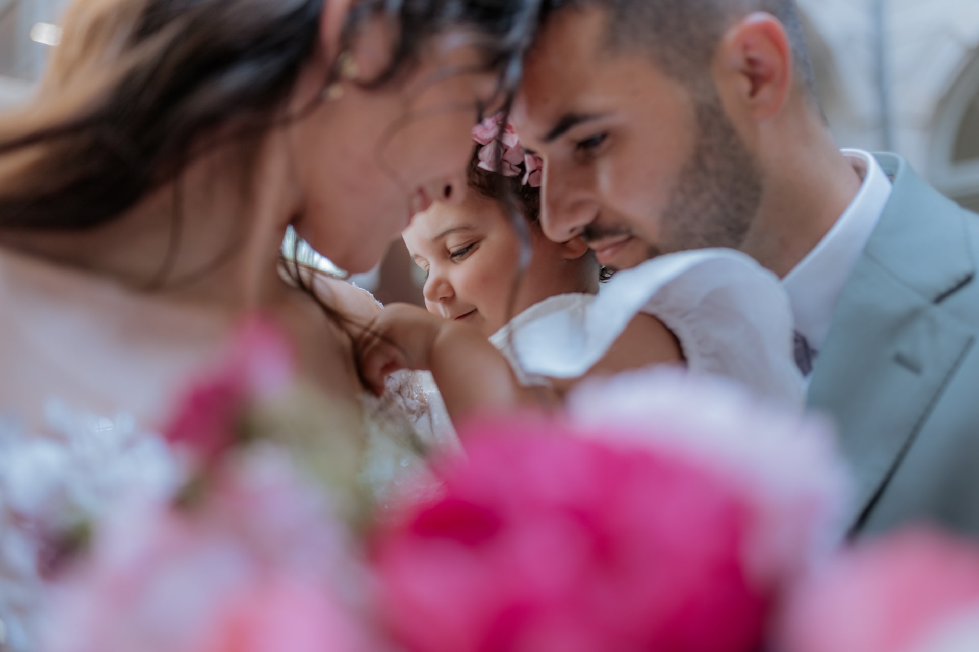 Un couple souriant avec un enfant lors d'un mariage, entouré de fleurs roses éclatantes, capturant un moment intime.