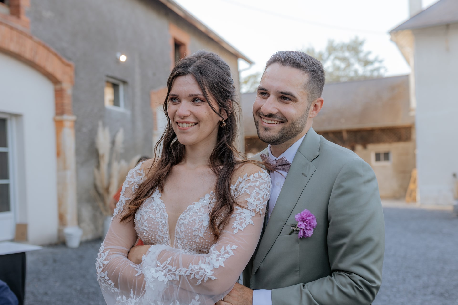 Mariés souriants devant le Domaine de Bourdale-Dufau, elle en robe élégante, lui en costume avec nœud papillon.