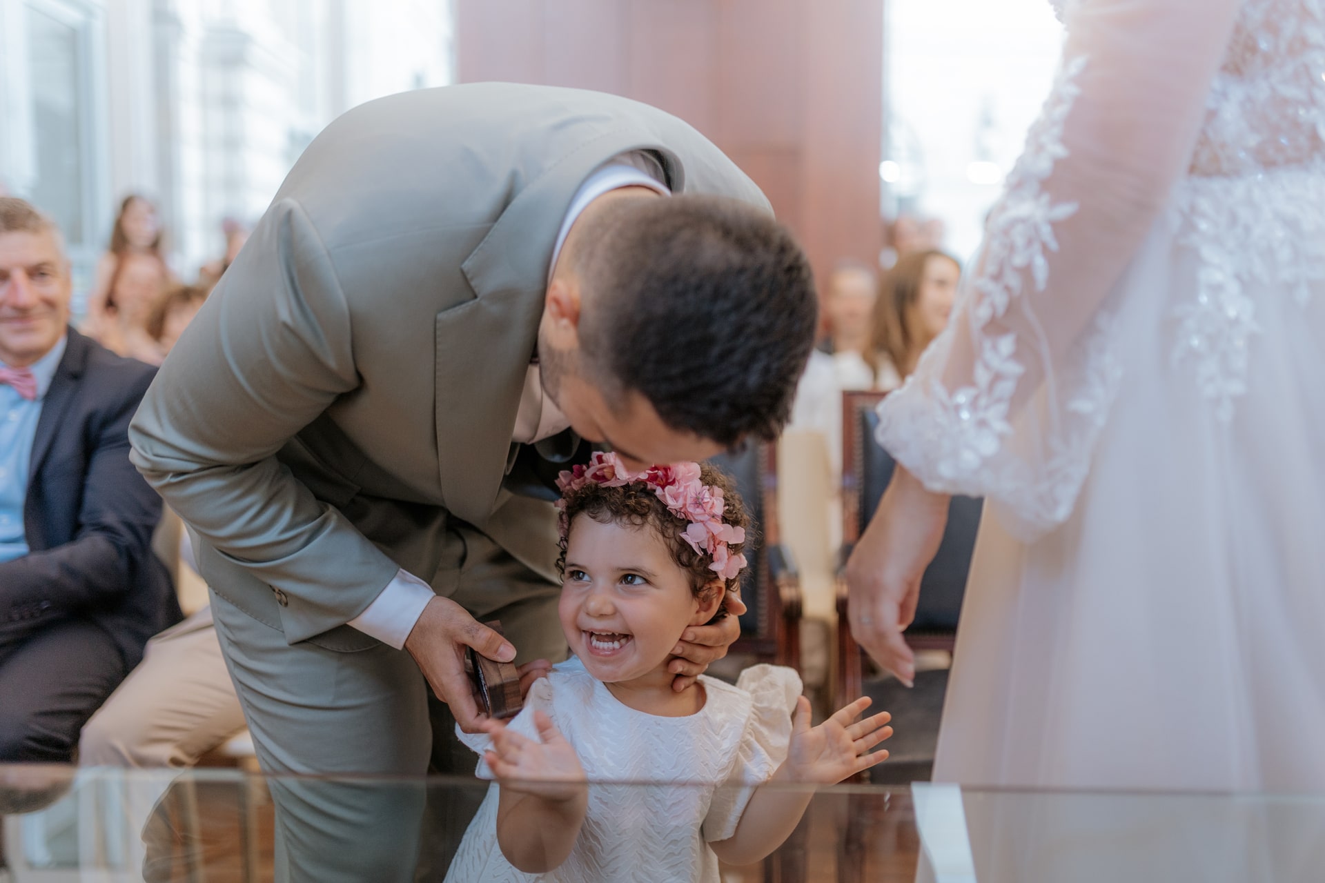 Un homme embrasse le front d'une fillette souriante avec une couronne de fleurs, lors d'une cérémonie de mariage.