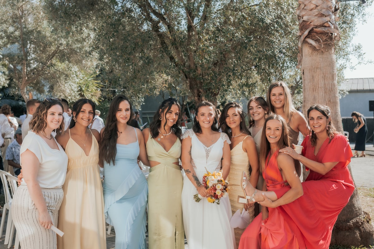 Mariée entourée d'amies en robes colorées sous un arbre à la Villa des 7 Moulins, mariage ensoleillé de Manon & Mickael.