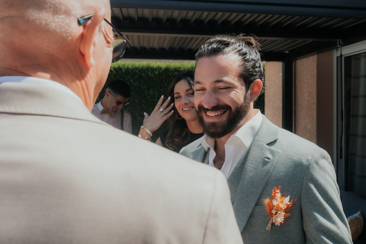 Mariage à la Villa des 7 Moulins, invité souriant en costume gris, décor floral. Ambiance joyeuse et conviviale.