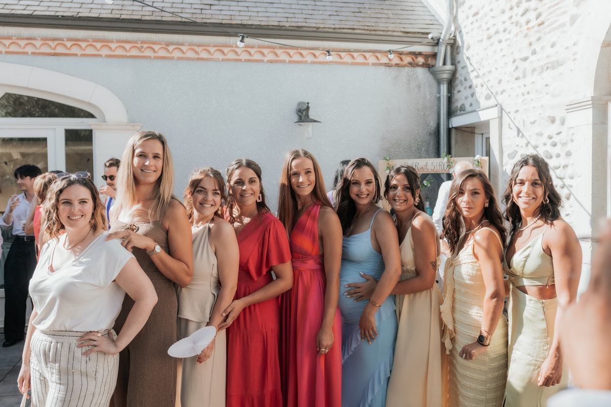 Groupe de femmes élégantes en vêtements festifs lors d'un mariage en plein air, souriantes et ensoleillées.