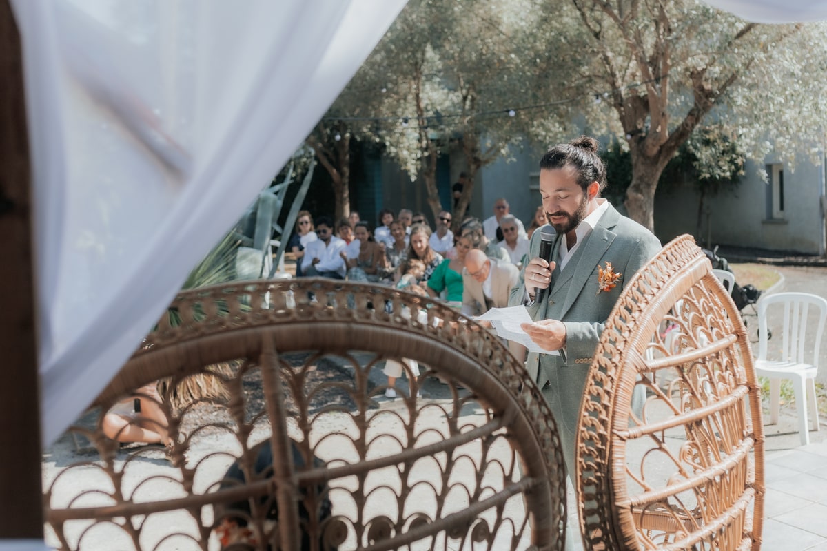 Homme en discours lors d'un mariage en plein air à la Villa des 7 Moulins, entouré d'invités sous le soleil.