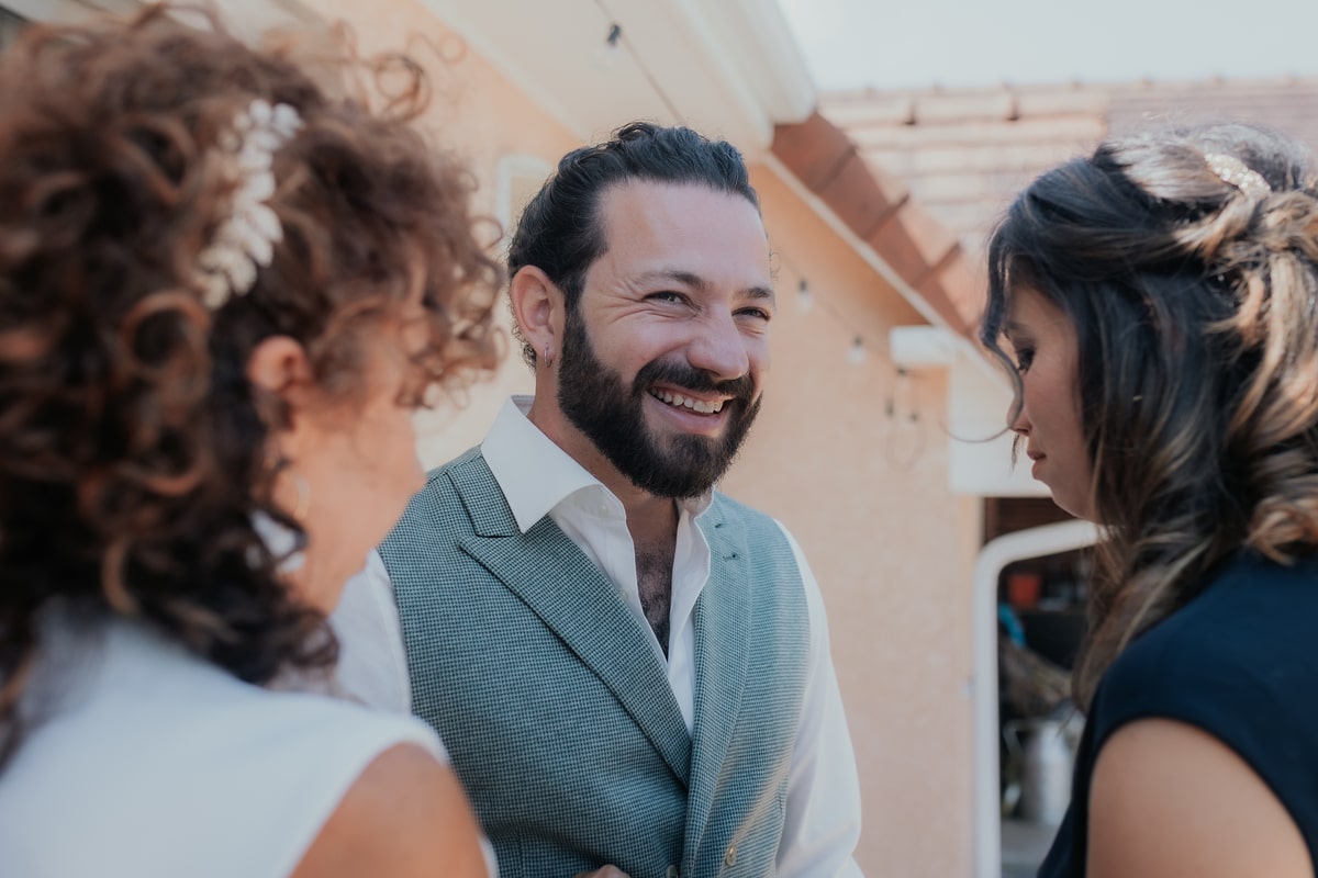 Homme souriant entouré de deux femmes lors d'un mariage en plein air à la Villa des 7 Moulins.