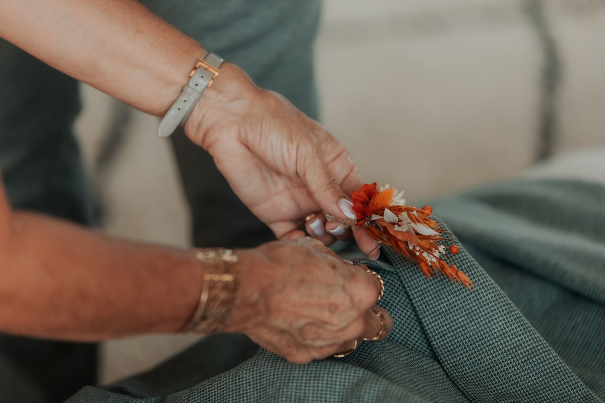 Une personne attache une boutonnière florale orange sur une veste à la Villa des 7 Moulins, mariage de Manon et Mickael.