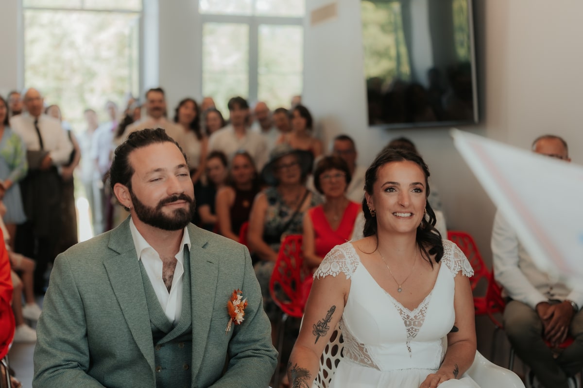 Mariage à la Villa des 7 Moulins : Le couple assis, entouré d'invités, écoute attentivement lors de la cérémonie.