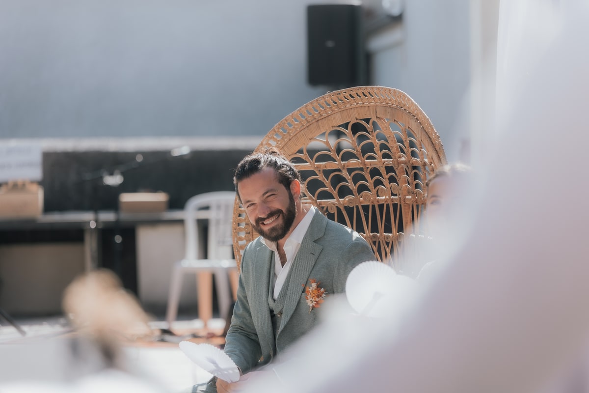 Marié souriant assis sur une chaise en osier lors d'une cérémonie ensoleillée à la Villa des 7 Moulins.