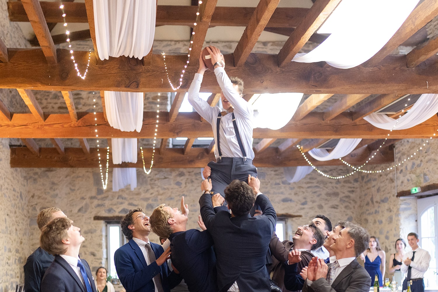 Invités en train de recevoir un ballon de rugby porté par leurs amis lors du mariage - Photographe mariage à Pau.
