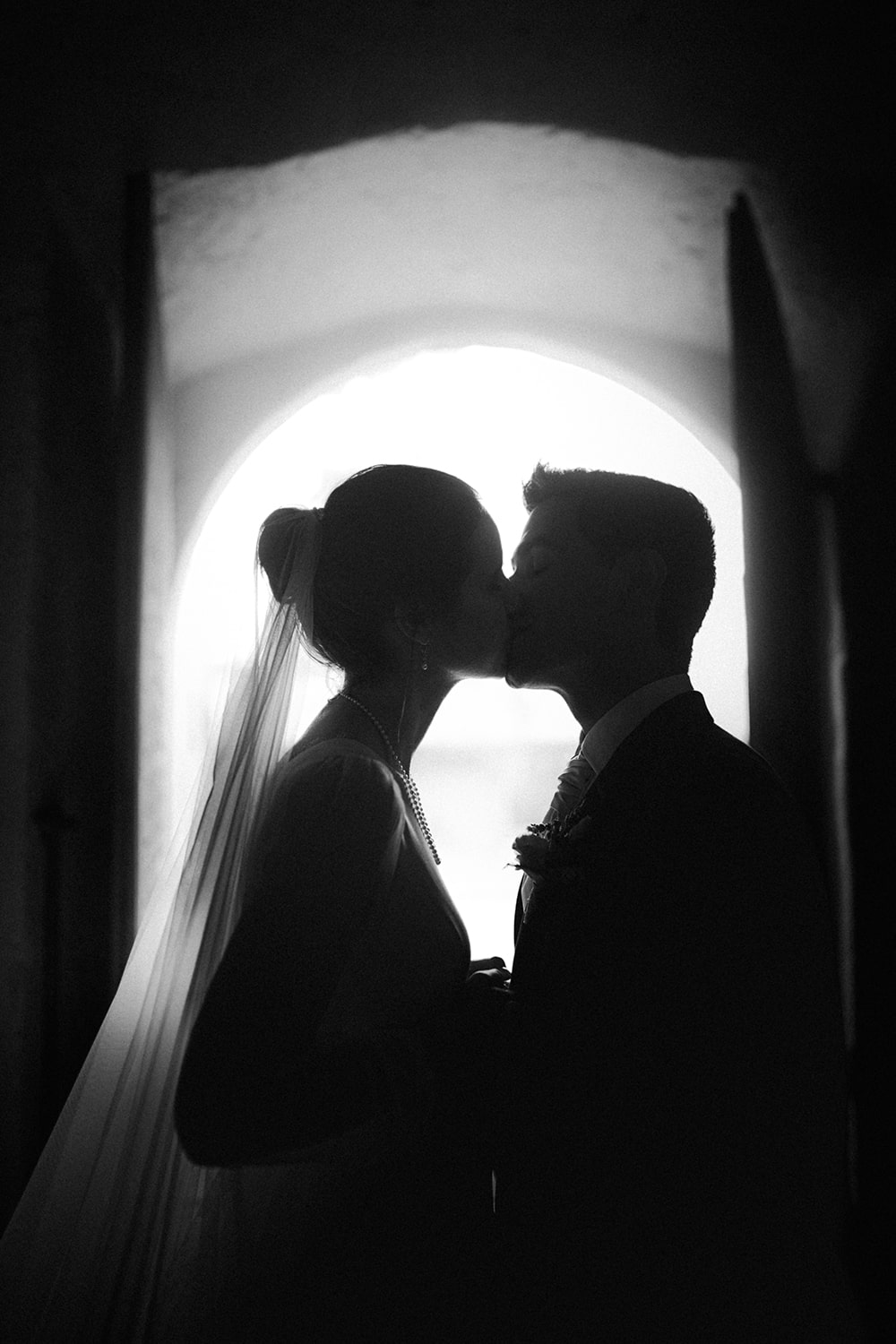 Photographie des mariés en noir et blanc en clair-obscur, s'embrassant - Photographe mariage à Pau.