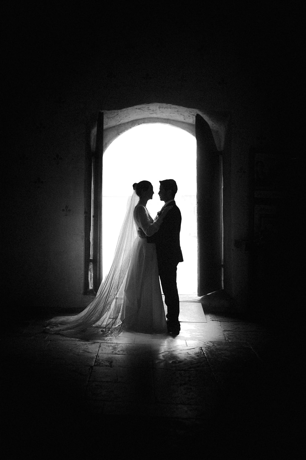 Photographie des mariés en noir et blanc en clair-obscur, se tenant l'un et l'autre et se regardant passionnément - Photographe mariage à Pau.
